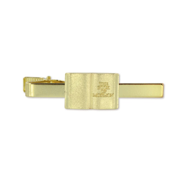 A gold-colored tie bar with 'The Book of Mormon' text inscribed on it.